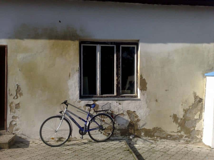 Staré murivo s poškodenou omietkou a bicyklom pred domom.