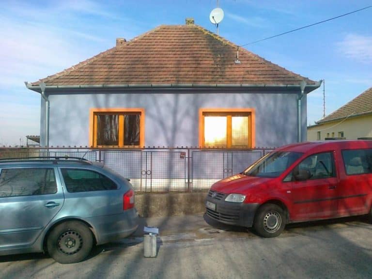 Dom s modrou fasádou a dvoma autami na ulici.