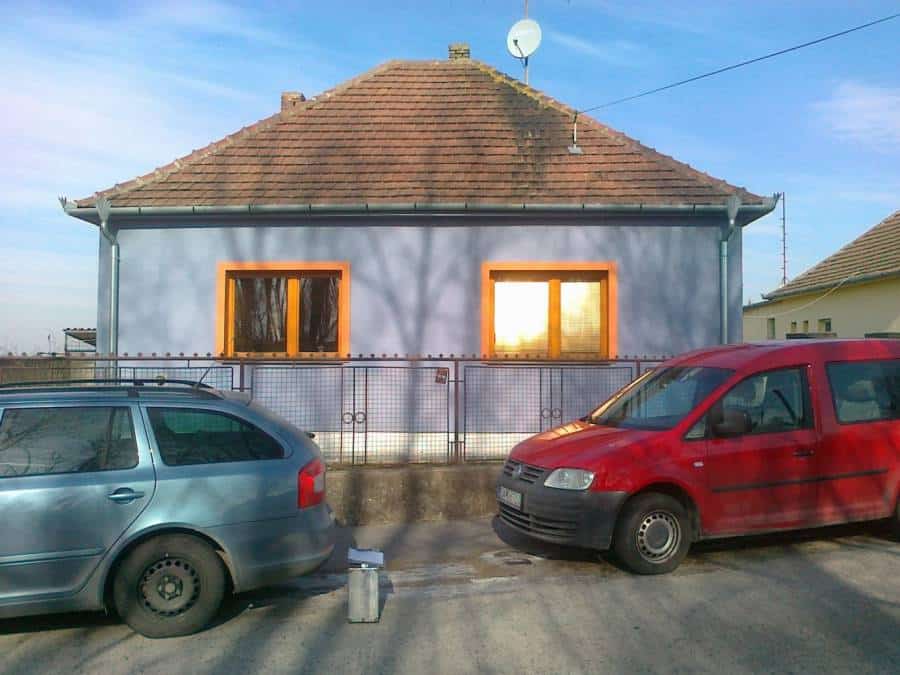 Dom so žltými oknami a červeným autom na ulici.