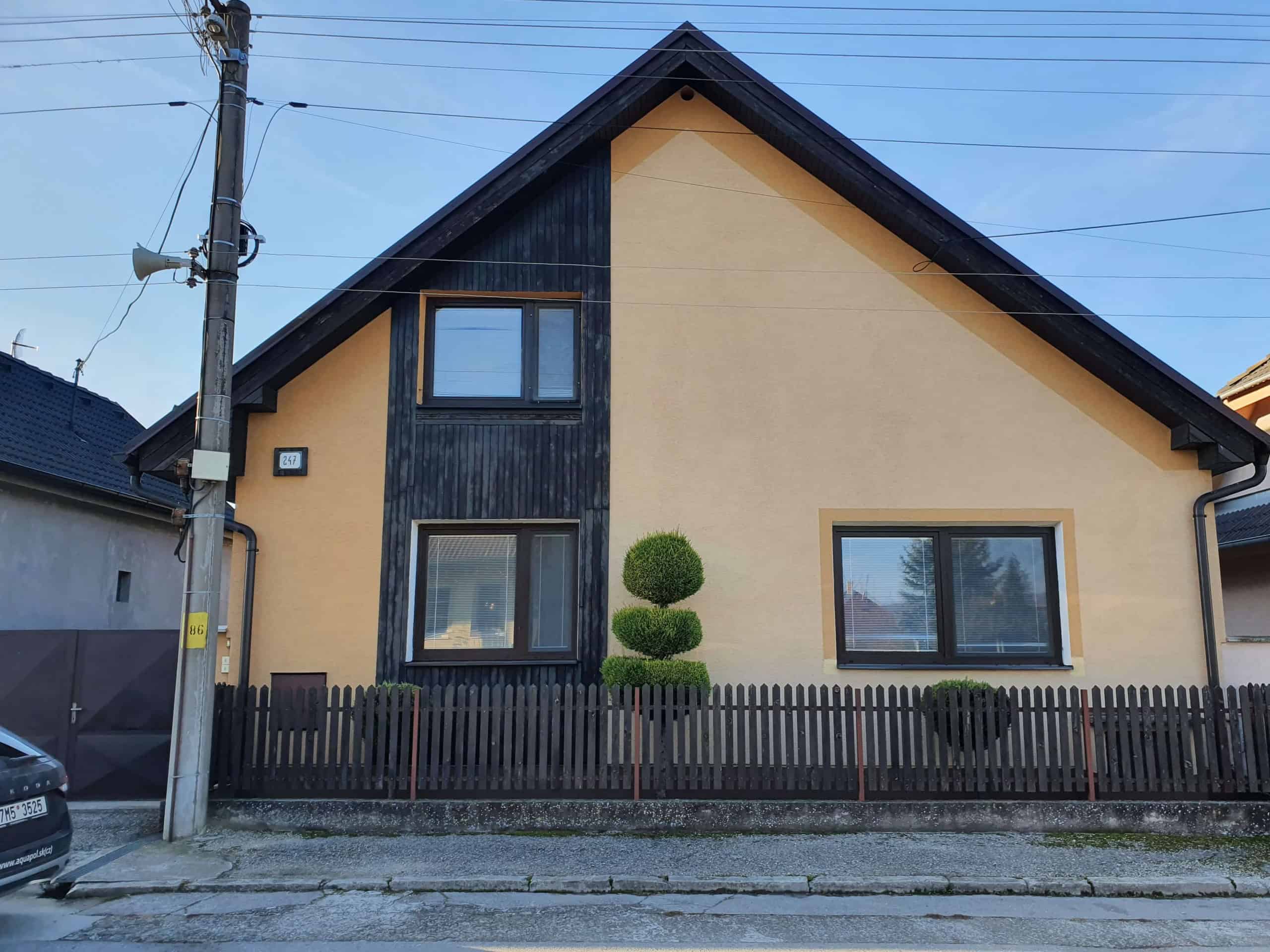 Moderný rodinný dom s čiernou a béžovou fasádou, záhradou a dreveným plotom.
