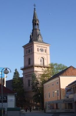 Historická veža kostola s vysokou špicatou strechou na modrom nebi.