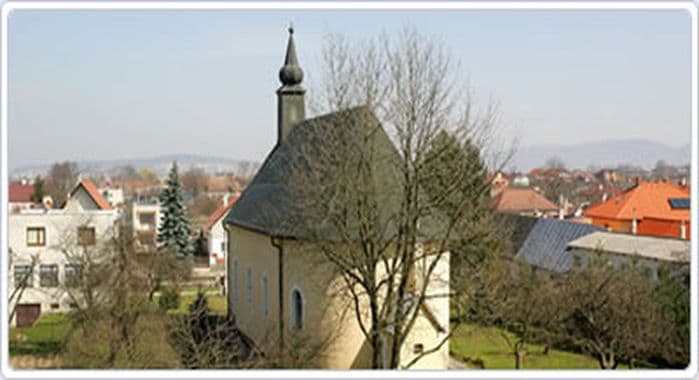 Historický kostol s vežou v obci Aquapol, okolie s domami a stromami.
