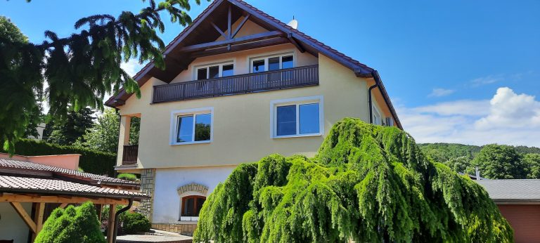 Moderný rodinný dom s veľkými oknami a zelenou záhradou pod modrou oblohou.