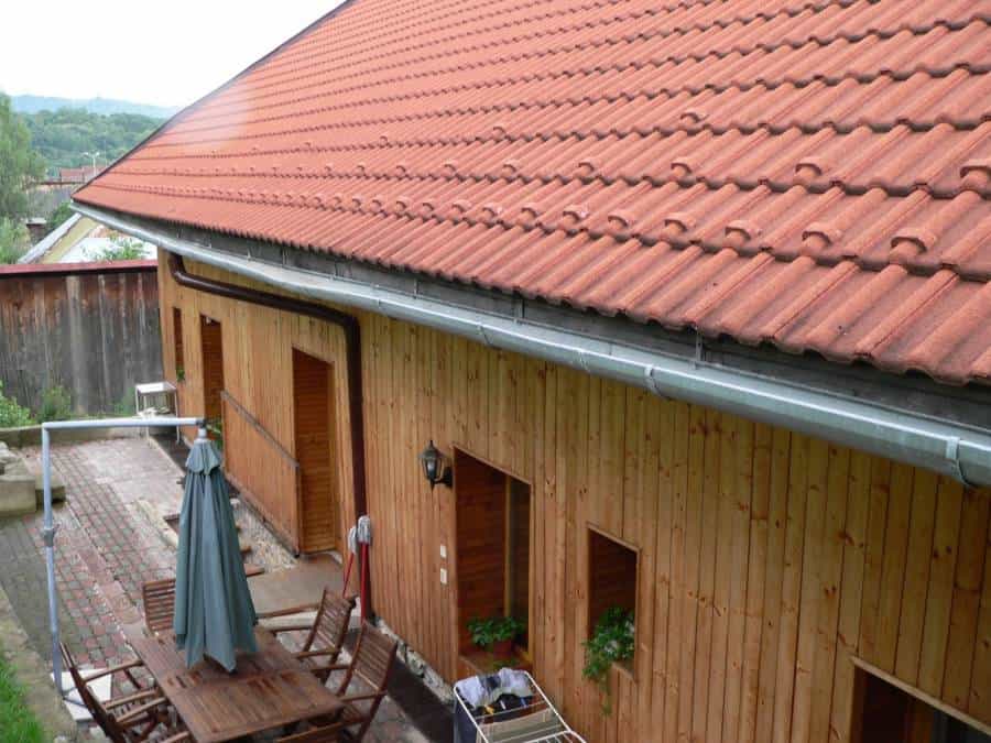 Drevený dom s červenou strechou, terasou a záhradou, ideálny pre relaxáciu a bývanie.