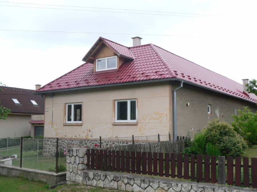 Rodinný dom s červenou strechou, vhodný pre rodiny, s peknou záhradou a bezpečným oplotením.