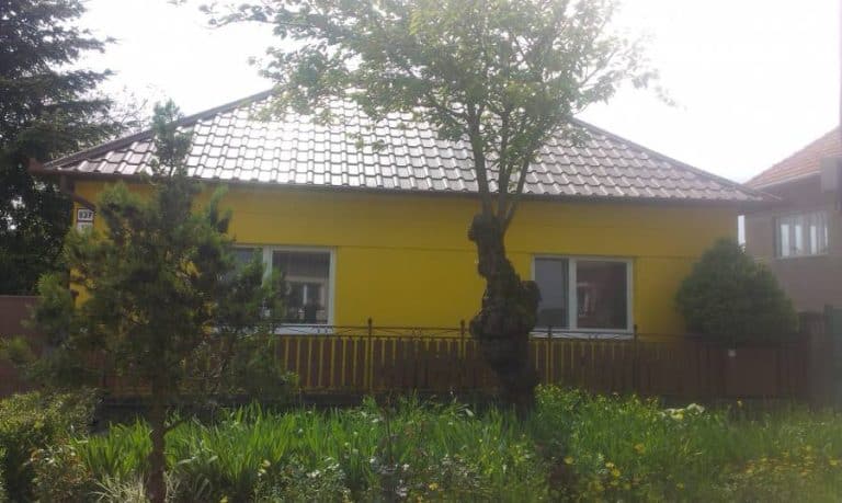 Dom s žltou fasádou a záhradou, ideálny pre rodinné bývanie, s upravenou záhradou a stromami.