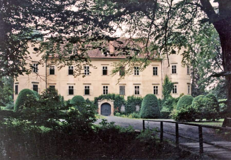 Historický kaštieľ obklopený zeleňou a stromami v parku.
